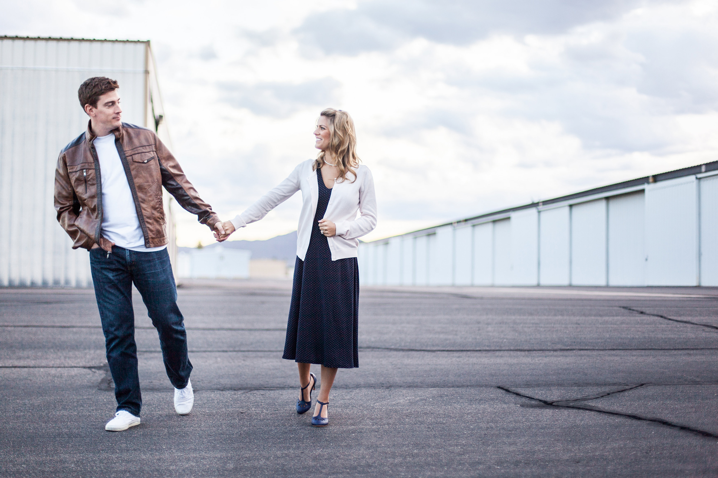 vintage styled couple holding hands and walking in airplane hangar alley