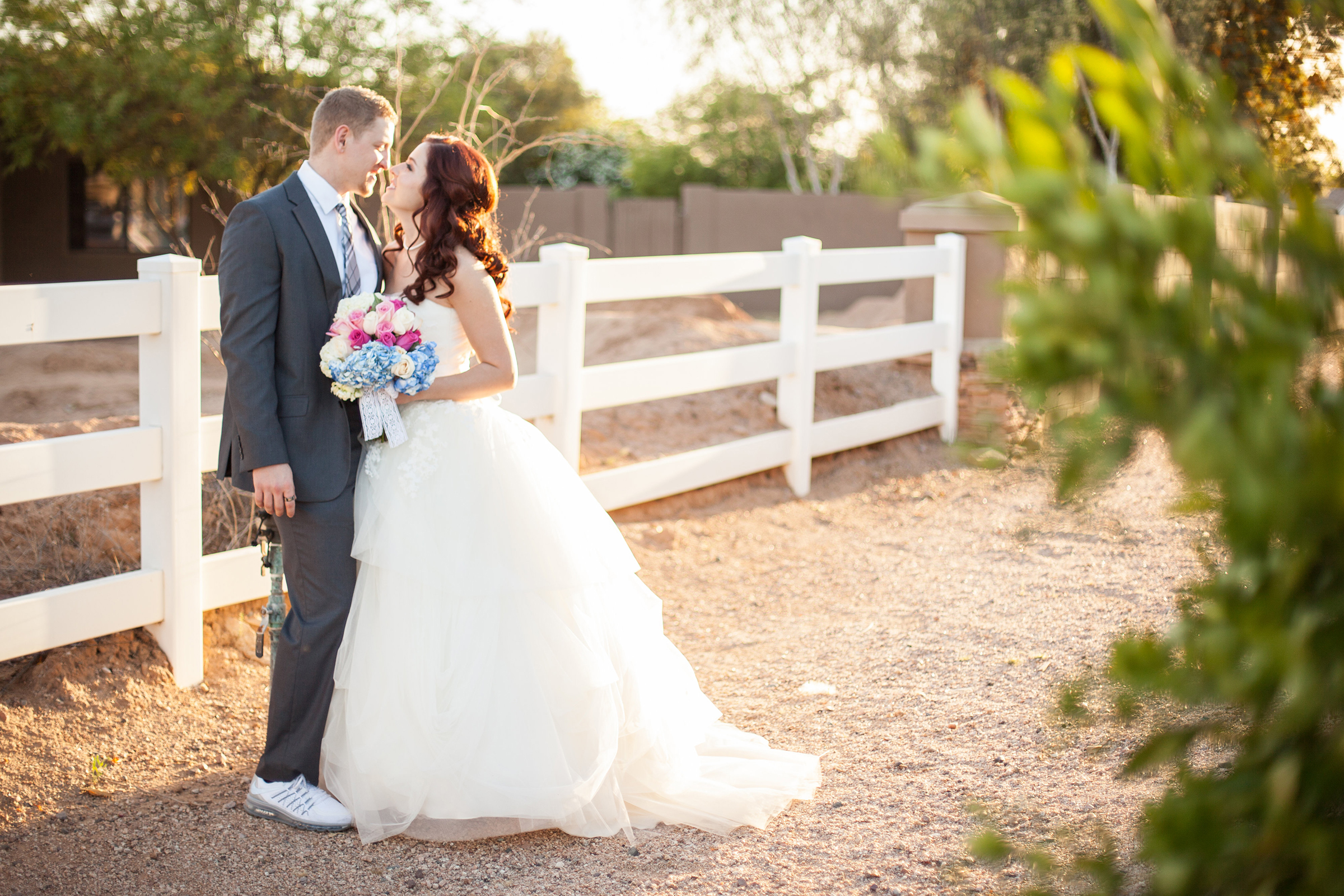 bride and groom by a white picket fence on their wedding day