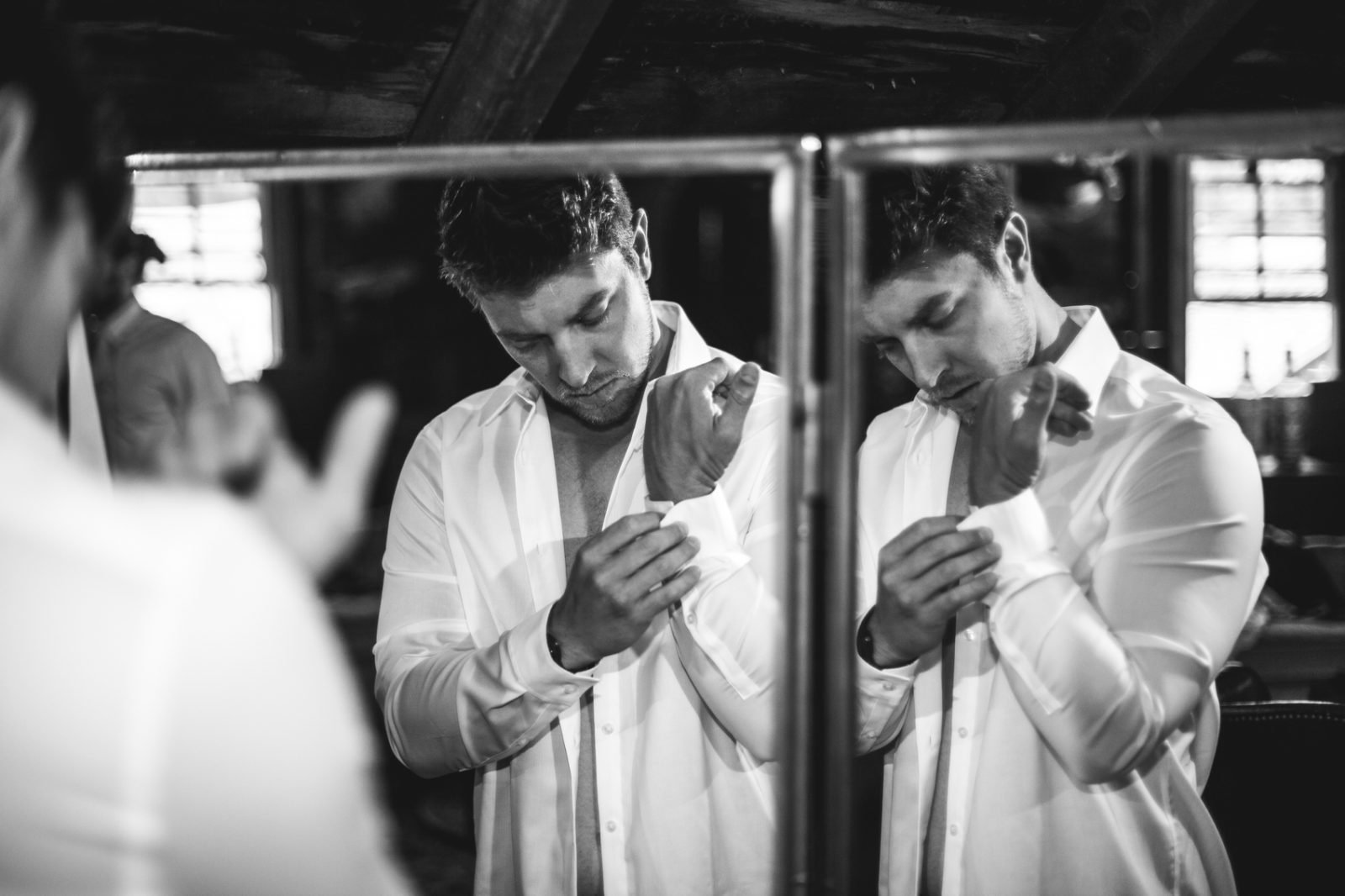 groom getting ready for wedding buttoning up shirt in black and white