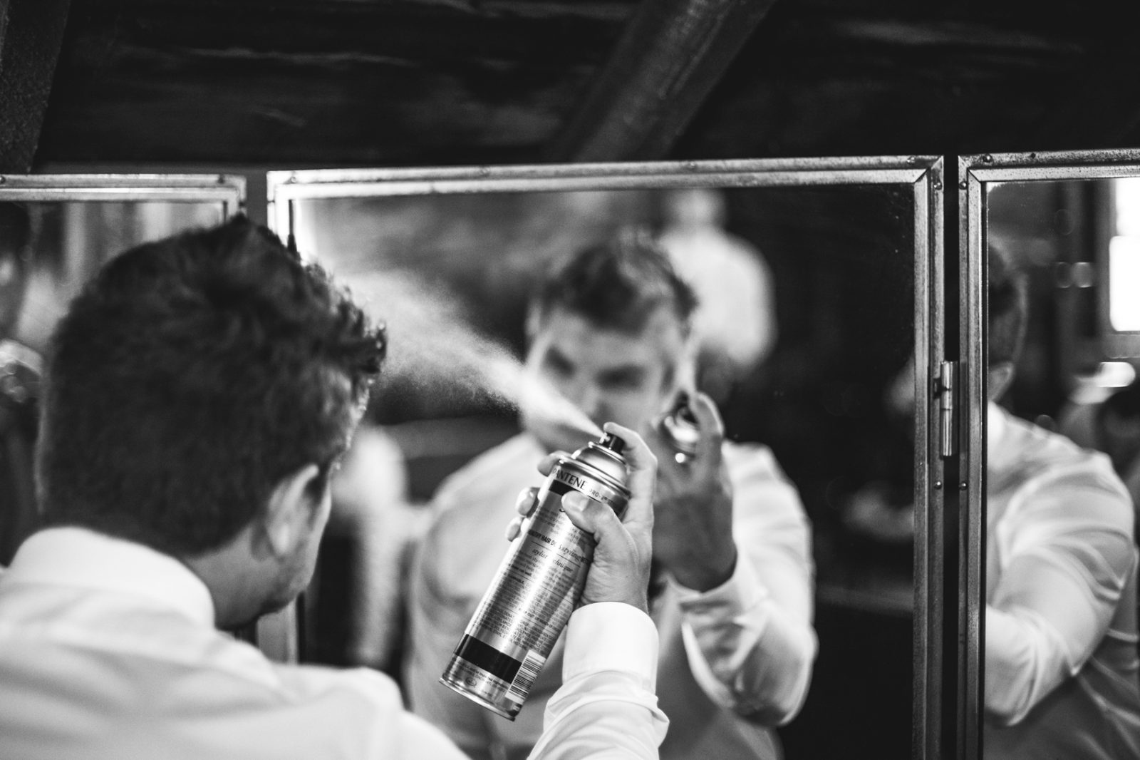 groom getting ready for wedding spraying hairspray in black and white