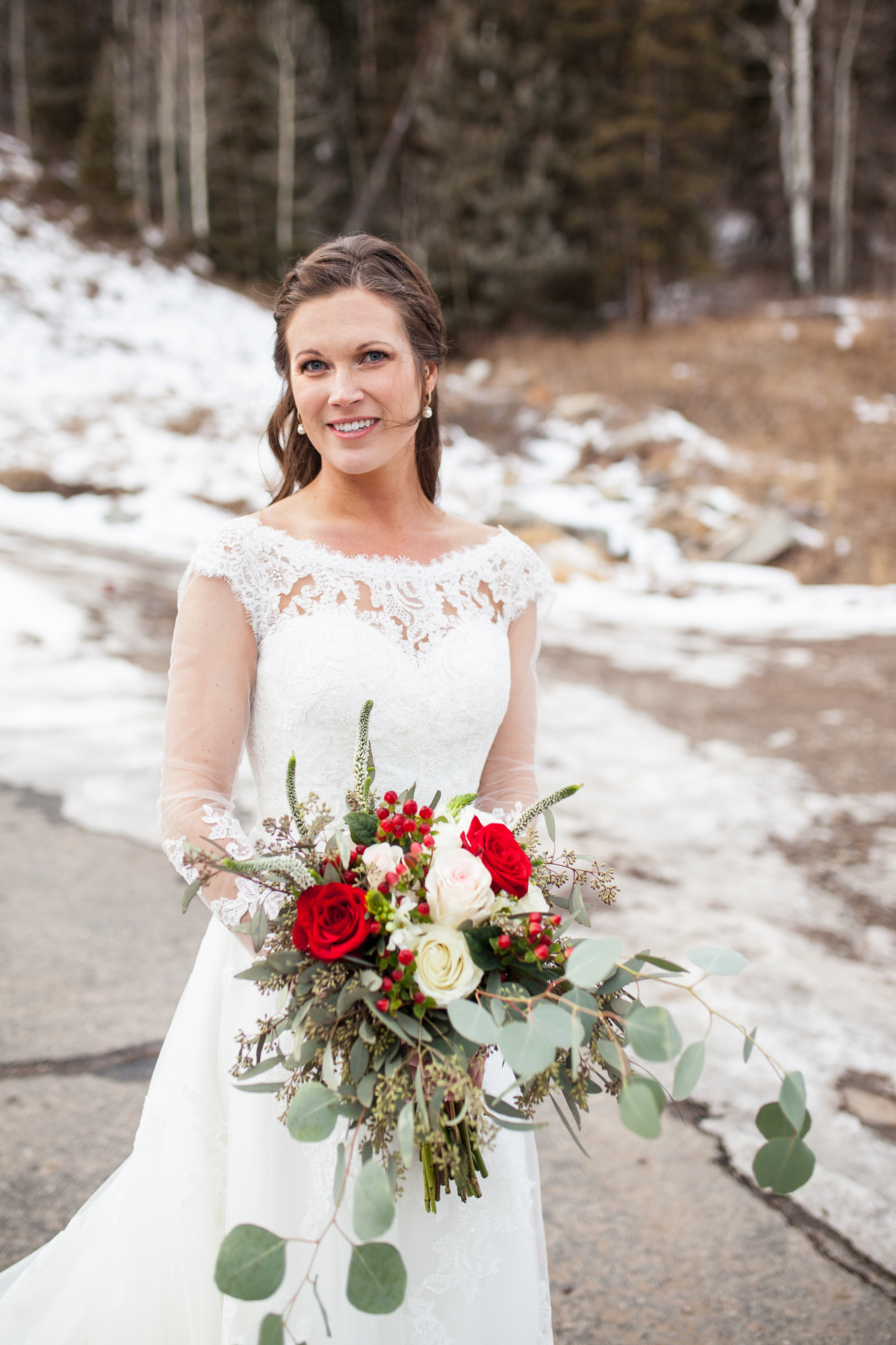 winter bride ideas with long sleeve lace sweetheart wedding dress and red rose bouquet in the snow