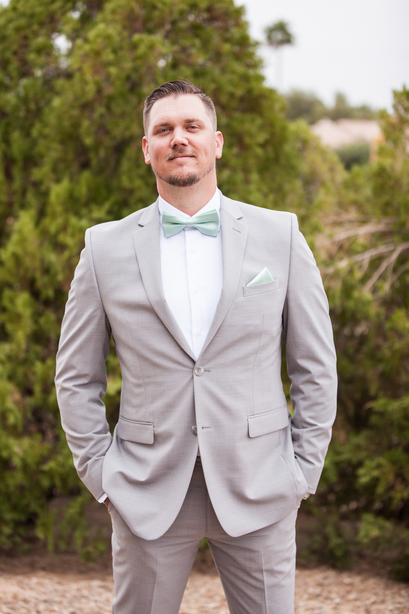groom in gray suit with teal blue bow tie and pocket square