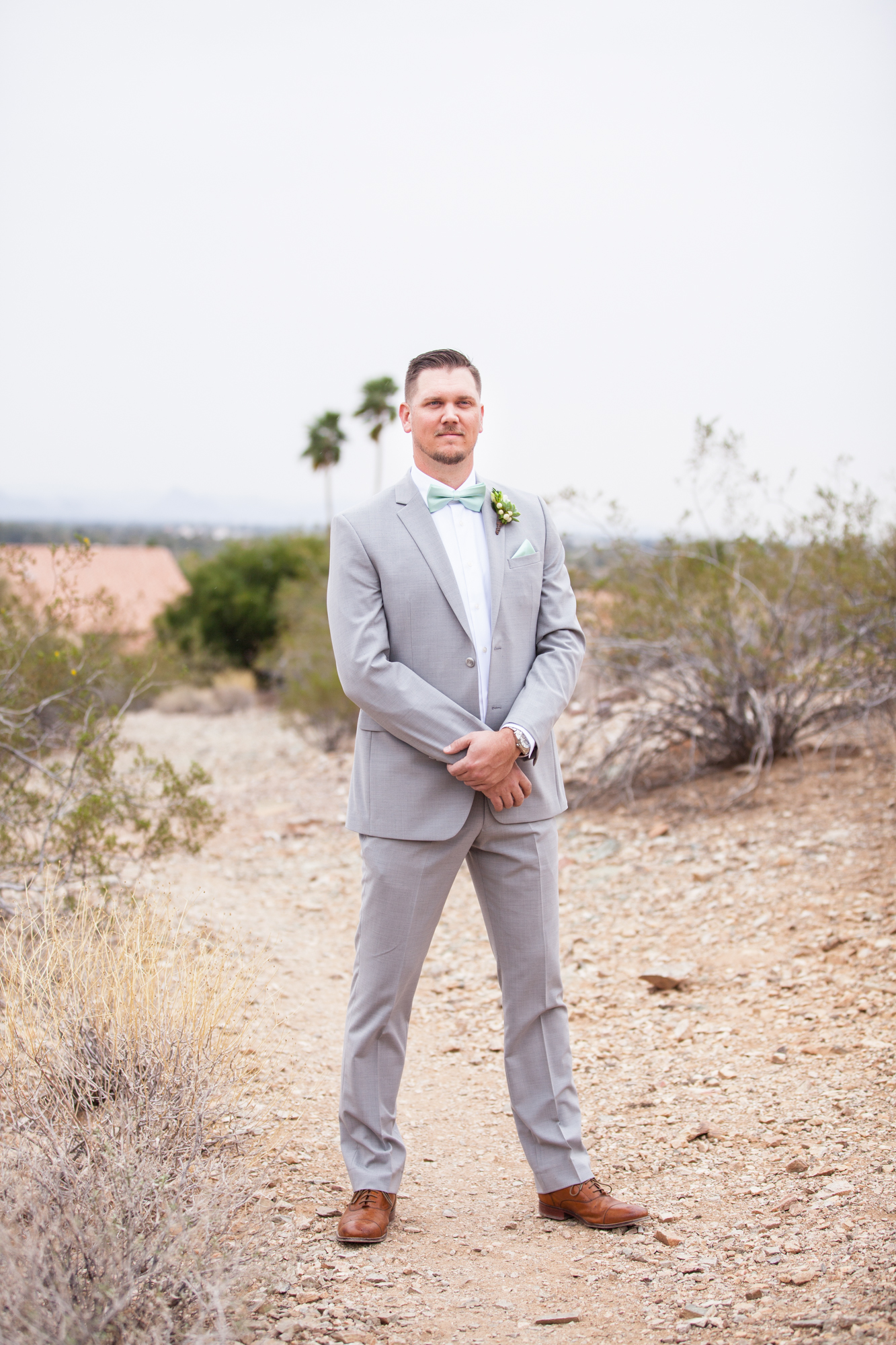 groom in gray suit with teal blue bow tie and pocket square waiting for first look with bride