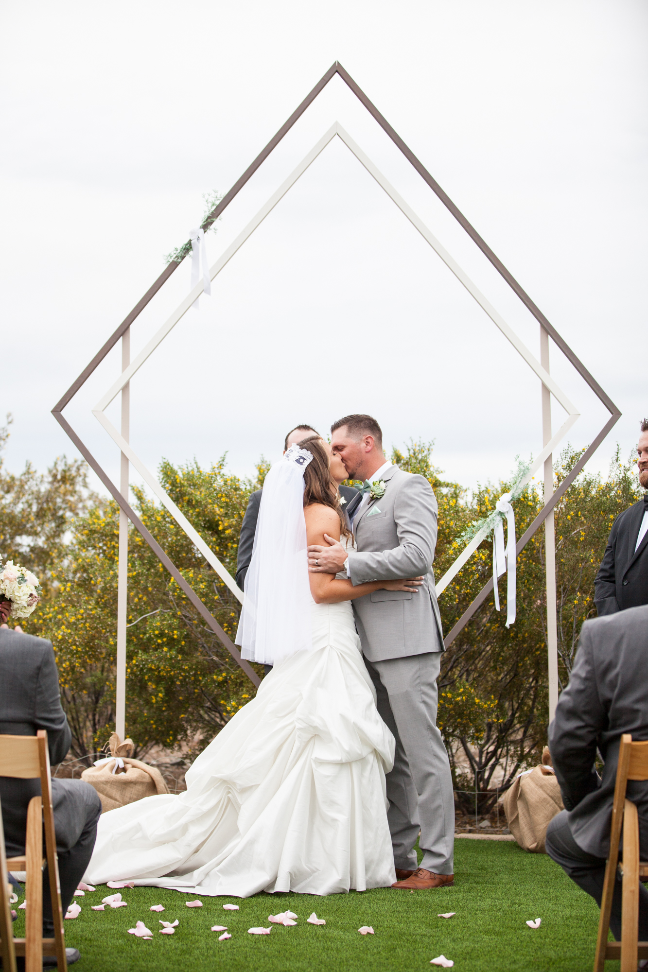 bride and groom first kiss at ceremony with wood diamond altar arbor